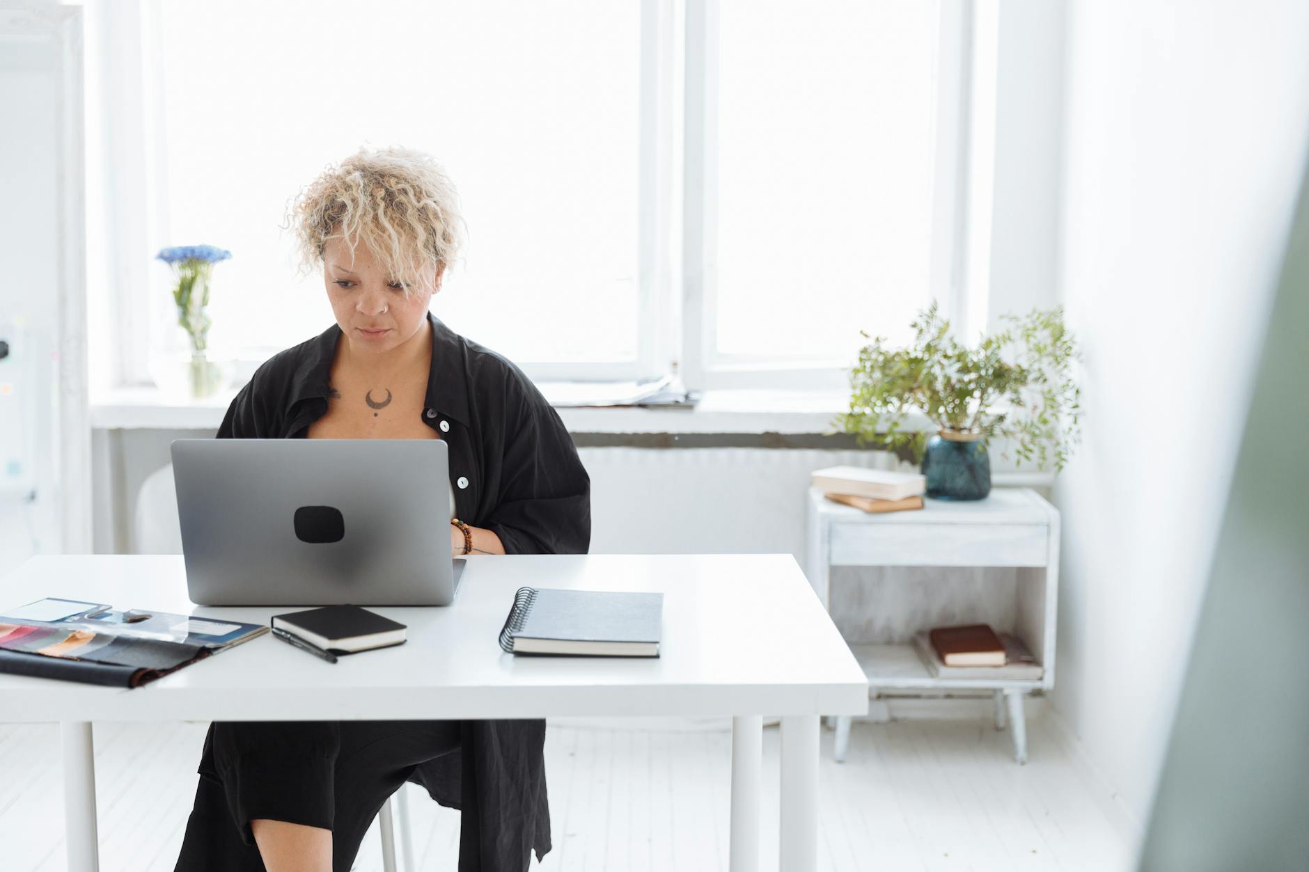 Woman focused on work at a bright, minimalist desk with a laptop and notebooks.