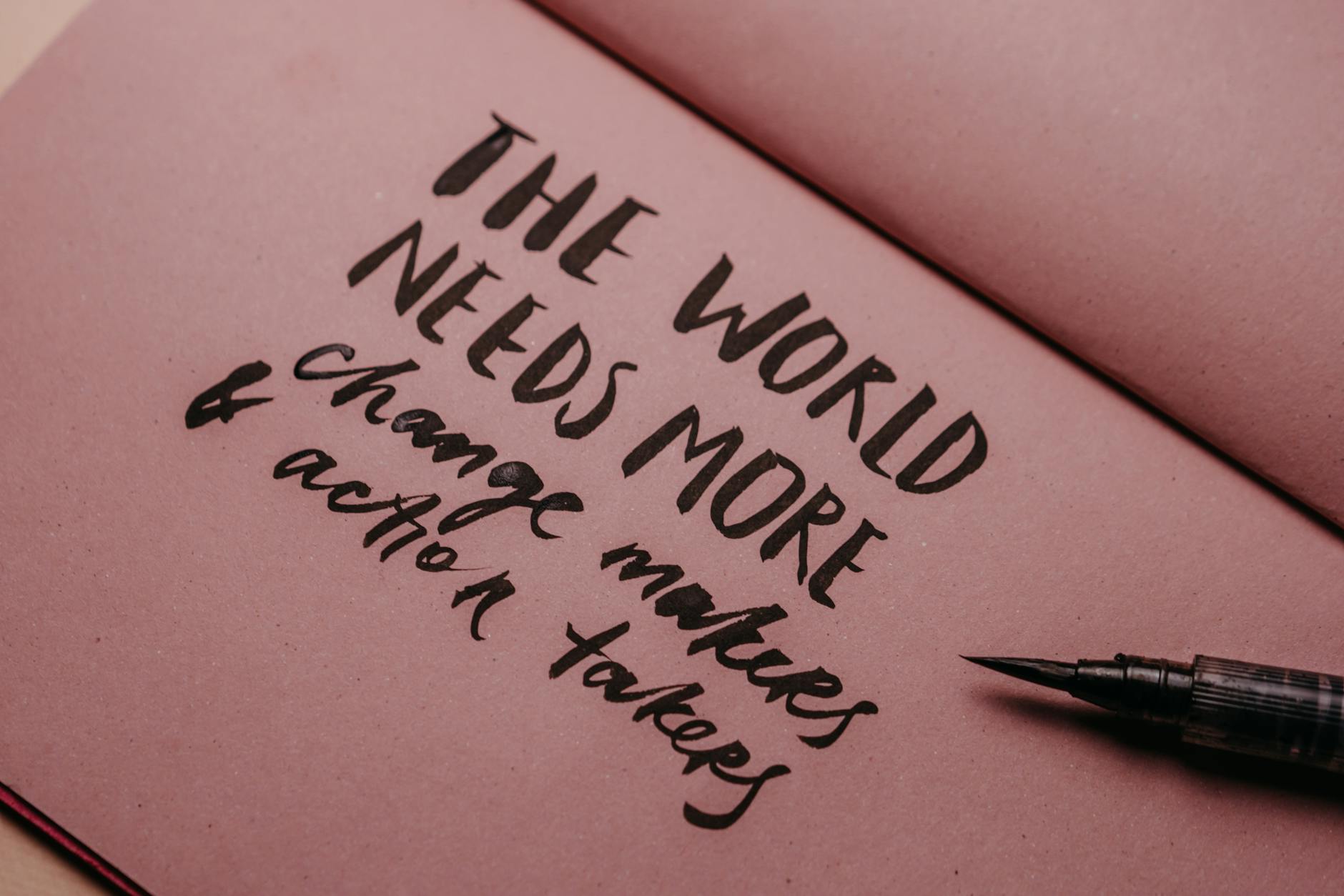 Close-up of a handwritten motivational quote on pink paper with a fountain pen.